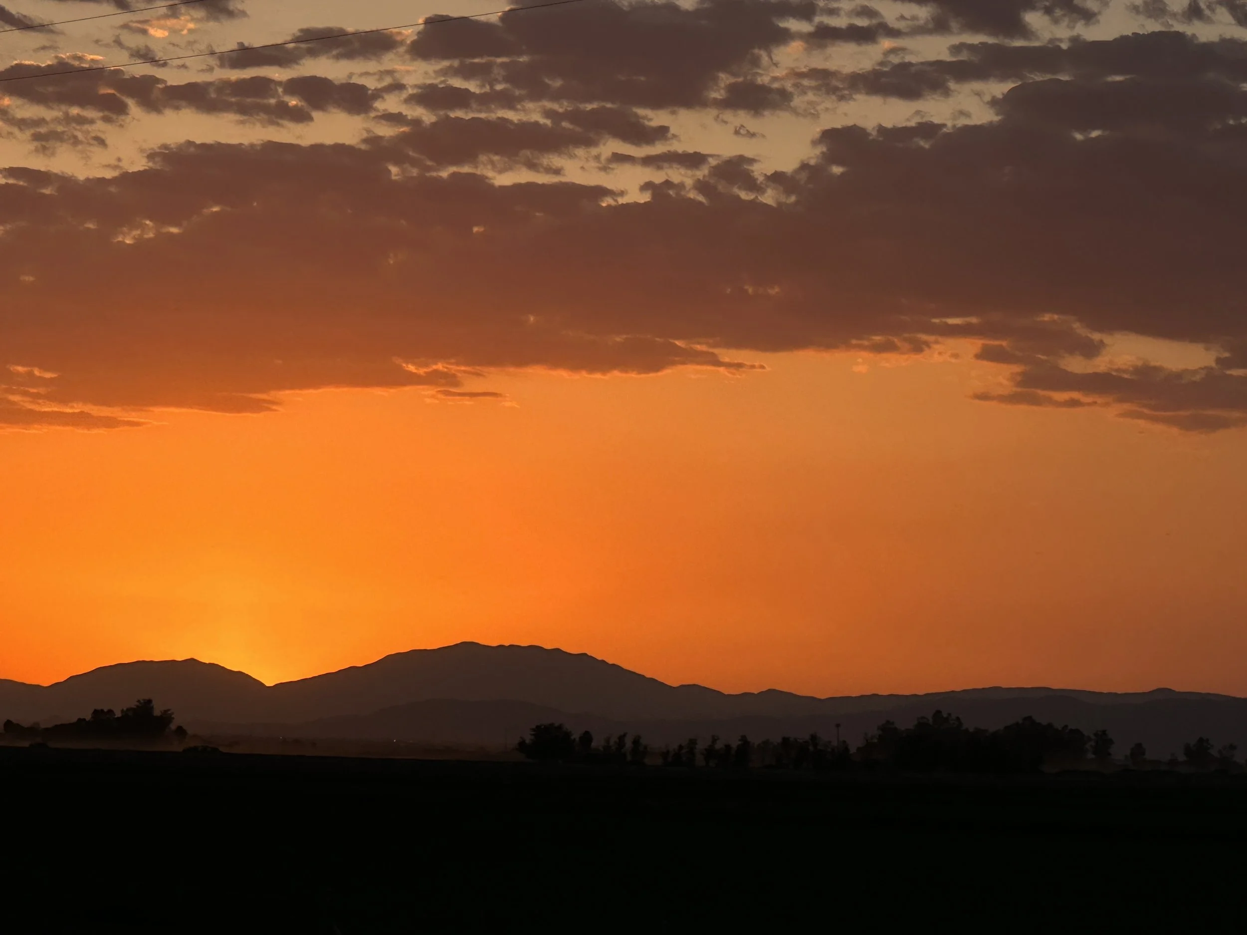 Sunset over mountains with orange sky and scattered clouds.