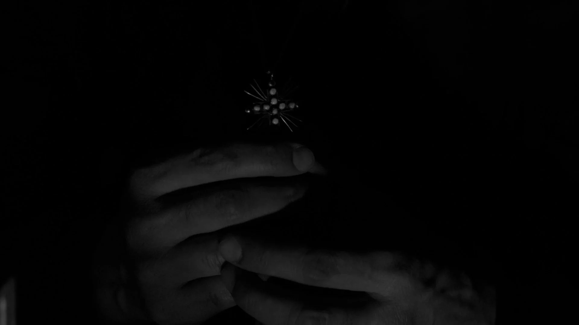 A person holding a small decorative beaded star ornament in a dark setting.
