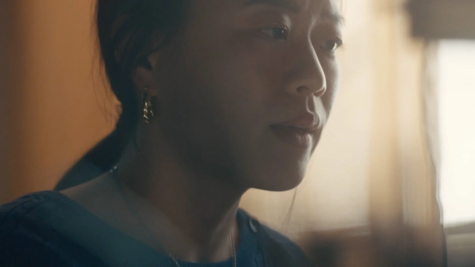 Close-up of a woman with dark hair and earrings looking out a window with natural light