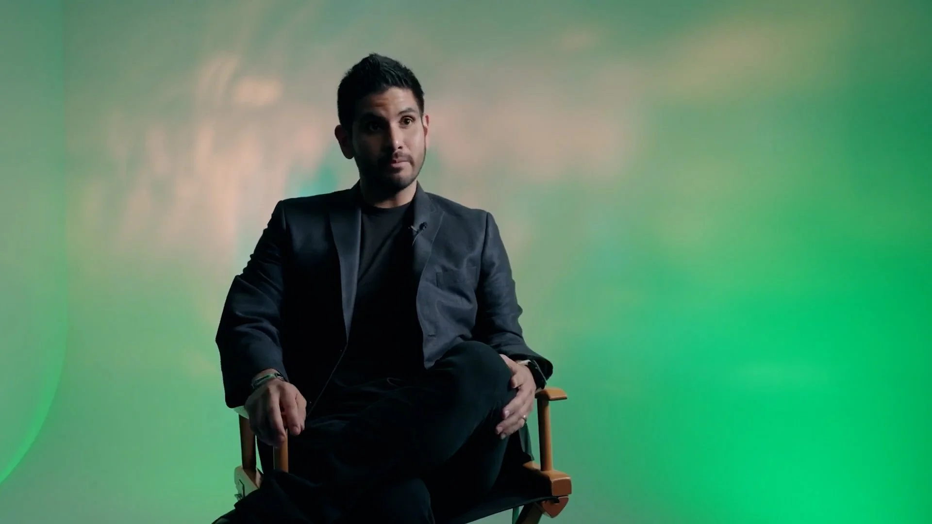 Man sitting on a director's chair with a colorful, abstract background.