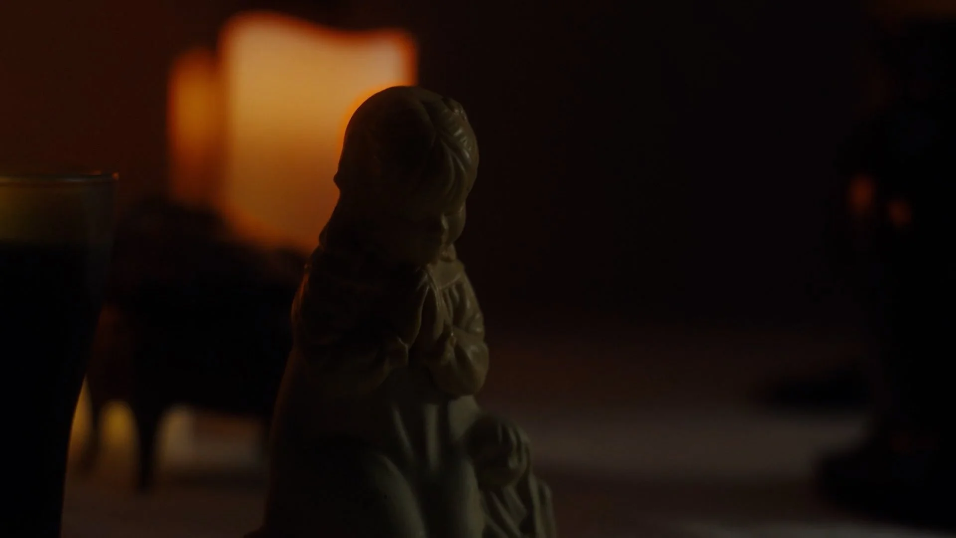 A shadowed figurine of a person kneeling with crossed arms, illuminated by a warm, blurred light in the background.