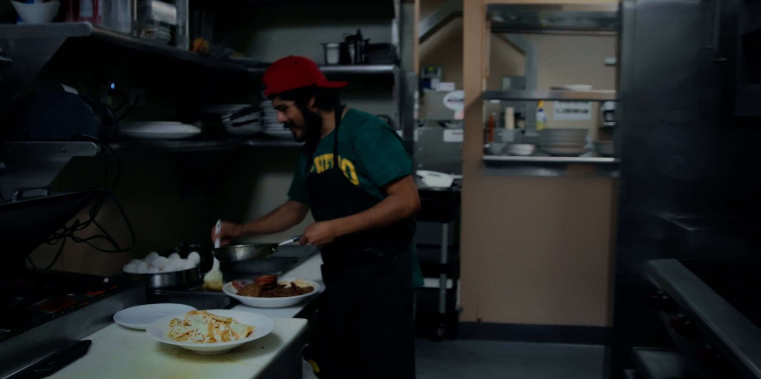 A man wearing a red cap and apron preparing food in a restaurant kitchen.