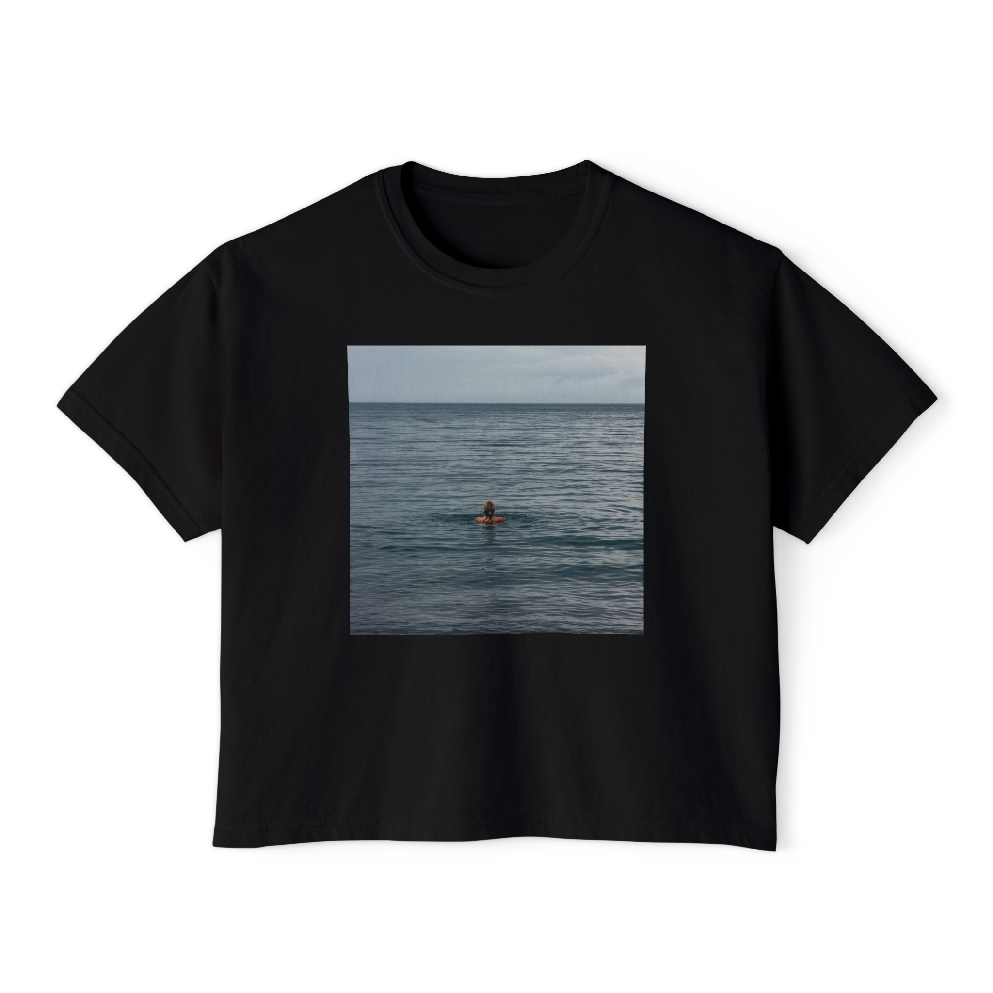 A black T-shirt with a rectangular photograph of a beach scene, featuring a person in the water, printed on the front.