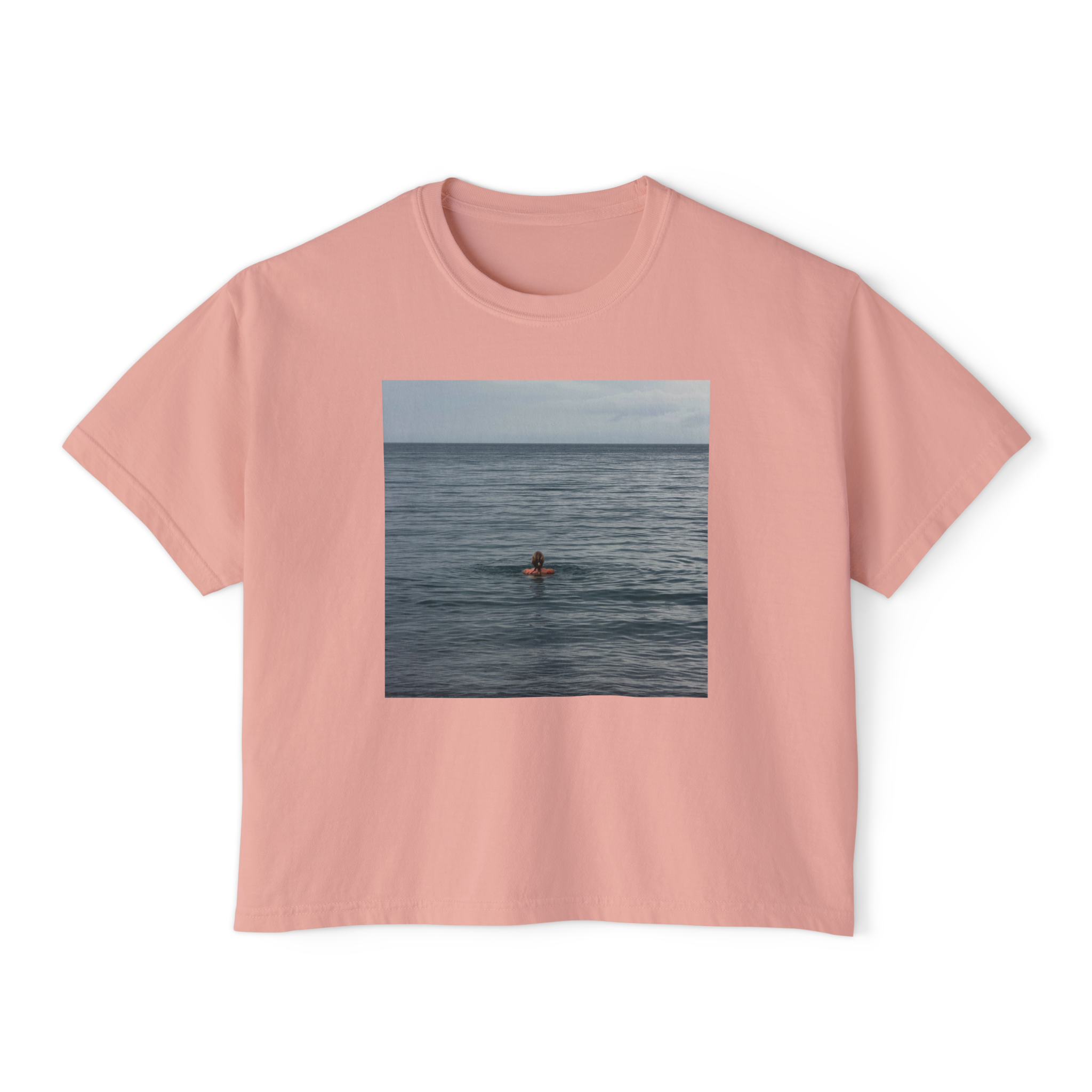 Pink T-shirt with a rectangular photo of a person surfing on the ocean printed on the front.