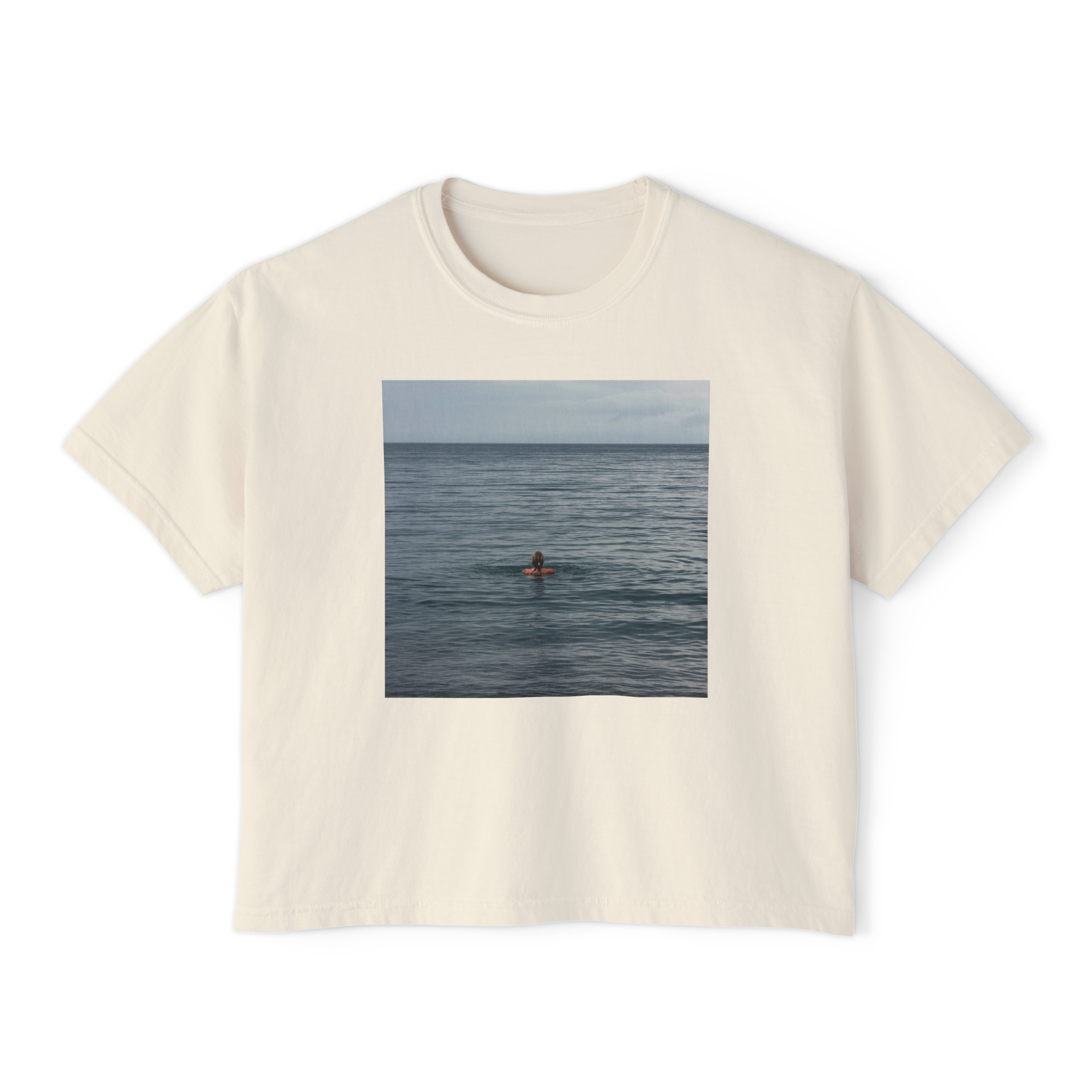 White T-shirt with a printed photo of a person lying on a surfboard in the ocean, overlooking the sea.