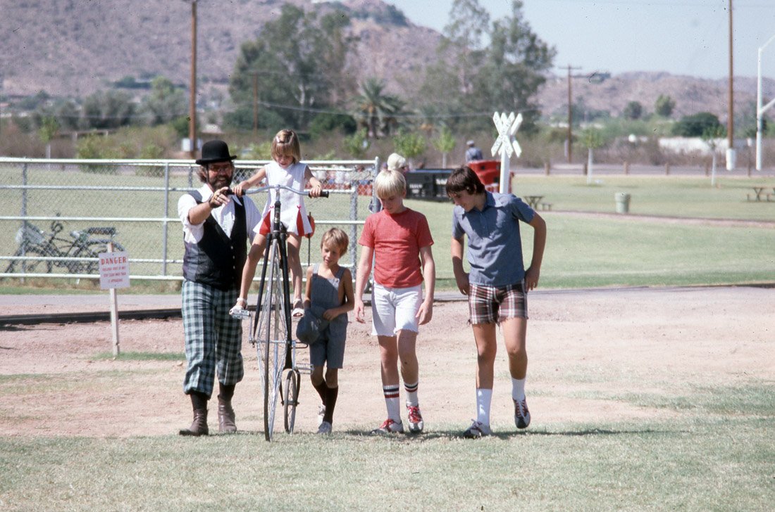Group of children walking on a field with an adult man holding a girl's bicycle