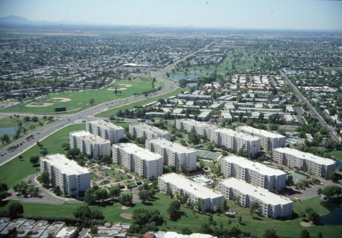 Aerial view of a city with a residential apartment complex, parks, a baseball field, lakes, and busy roads.