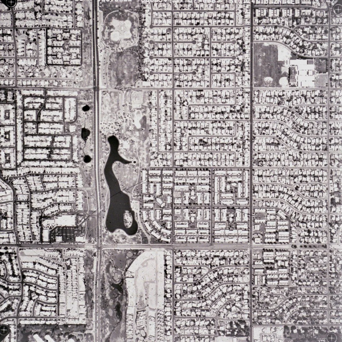 Aerial view of a residential neighborhood with roads, houses, and a central park with lakes.