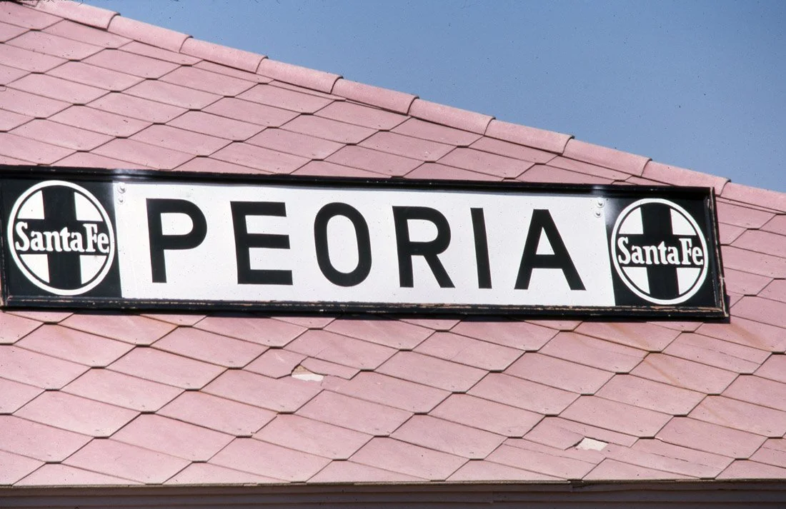 Sign for Peoria with Santa Fe logos on a pink tiled roof.