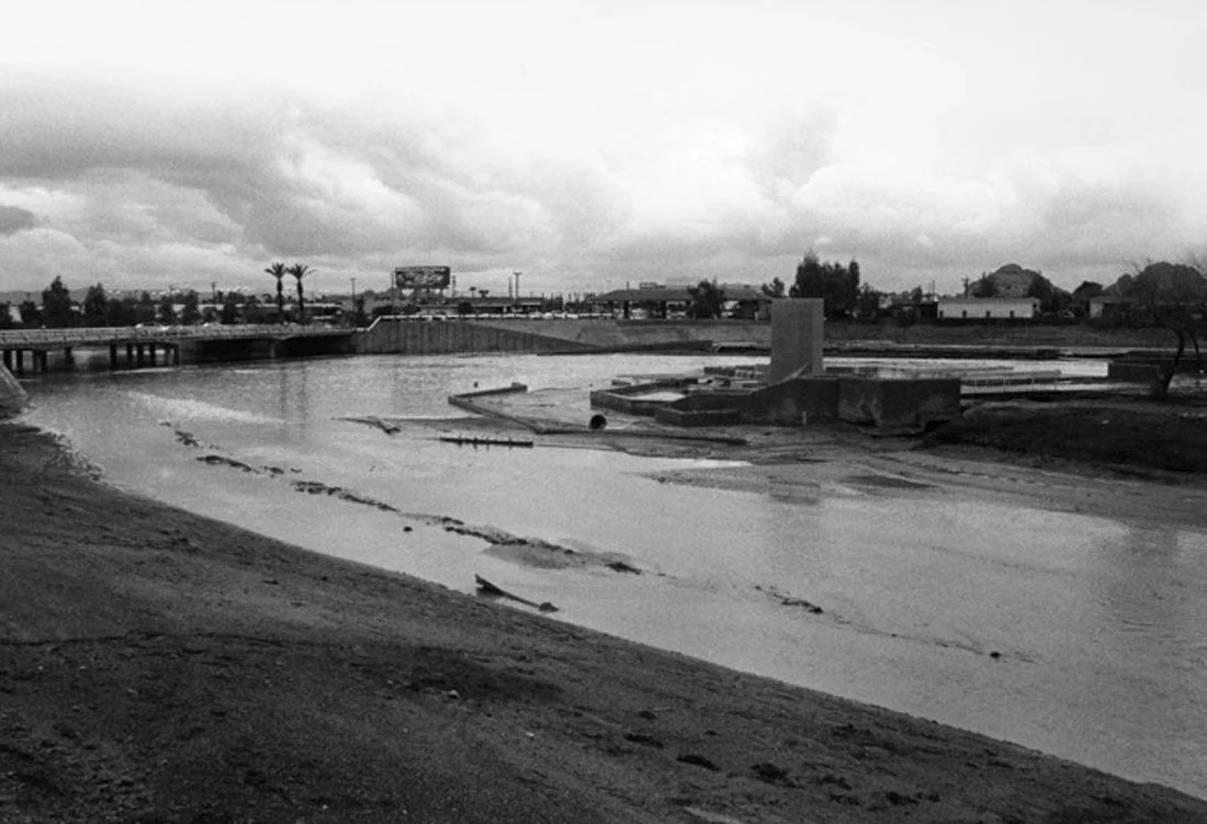 A black and white photo of an empty water park with a large pool, empty walkways, and overcast skies.