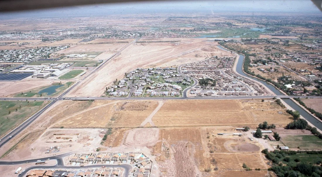 Aerial view of an urban and suburban area with construction sites, roads, residential neighborhoods, and a river.