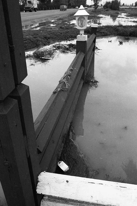 Flooded sidewalk with displaced fence and lamp post near water