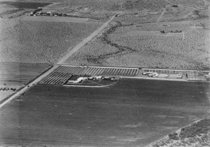 Aerial view of farmland with fields, trees, roads, and a large building complex.