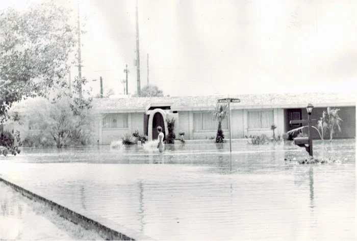 A house underwater, with floodwaters reaching up to the windows and a boat in the yard.