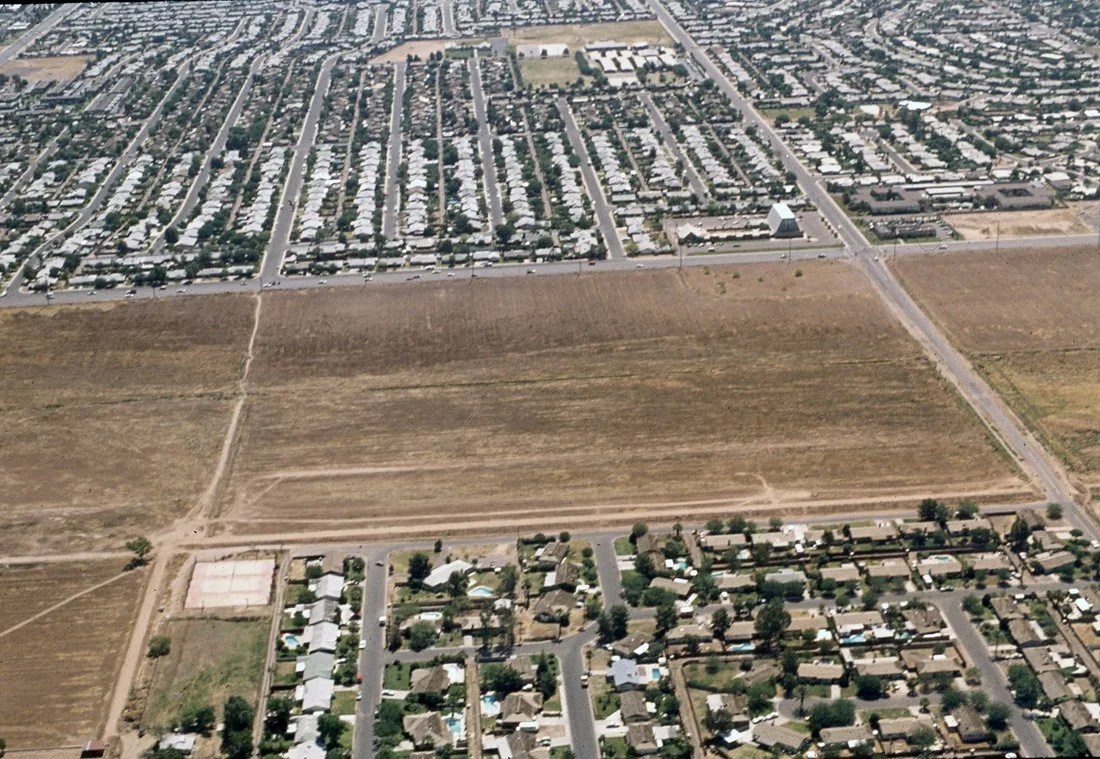 Aerial view of a suburban neighborhood with houses, streets, and open fields.