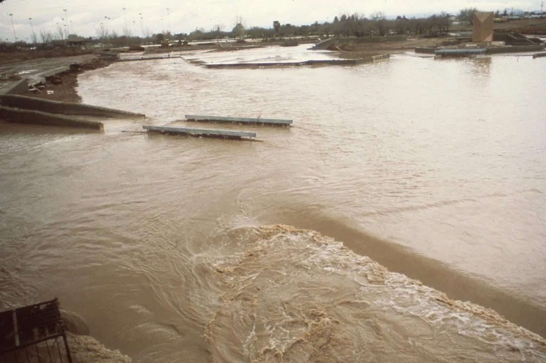 Flooded area with muddy water and partially submerged structures, overcast sky.