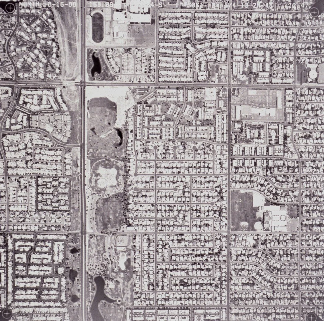 A black and white aerial view of an urban area with residential neighborhoods, roads, and lakes.