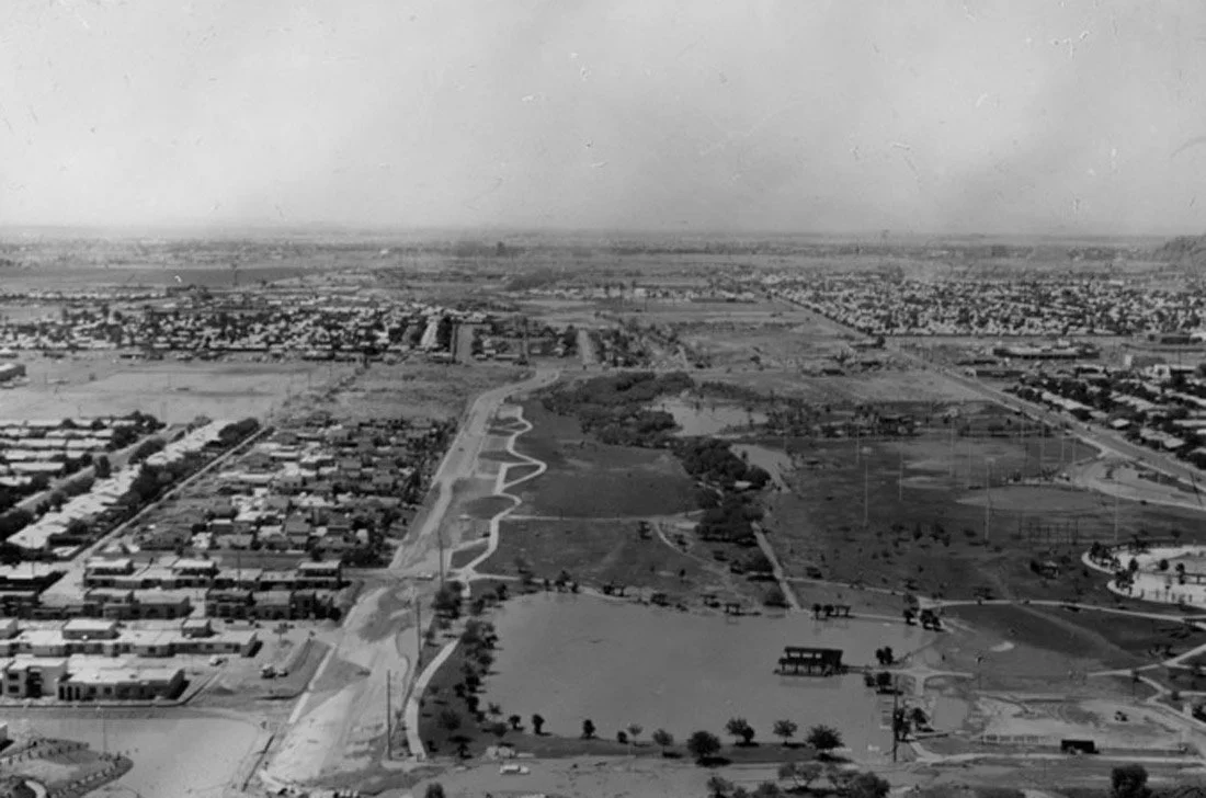 An aerial black and white photograph of an urban park with walking paths, trees, and surrounding residential and commercial areas.