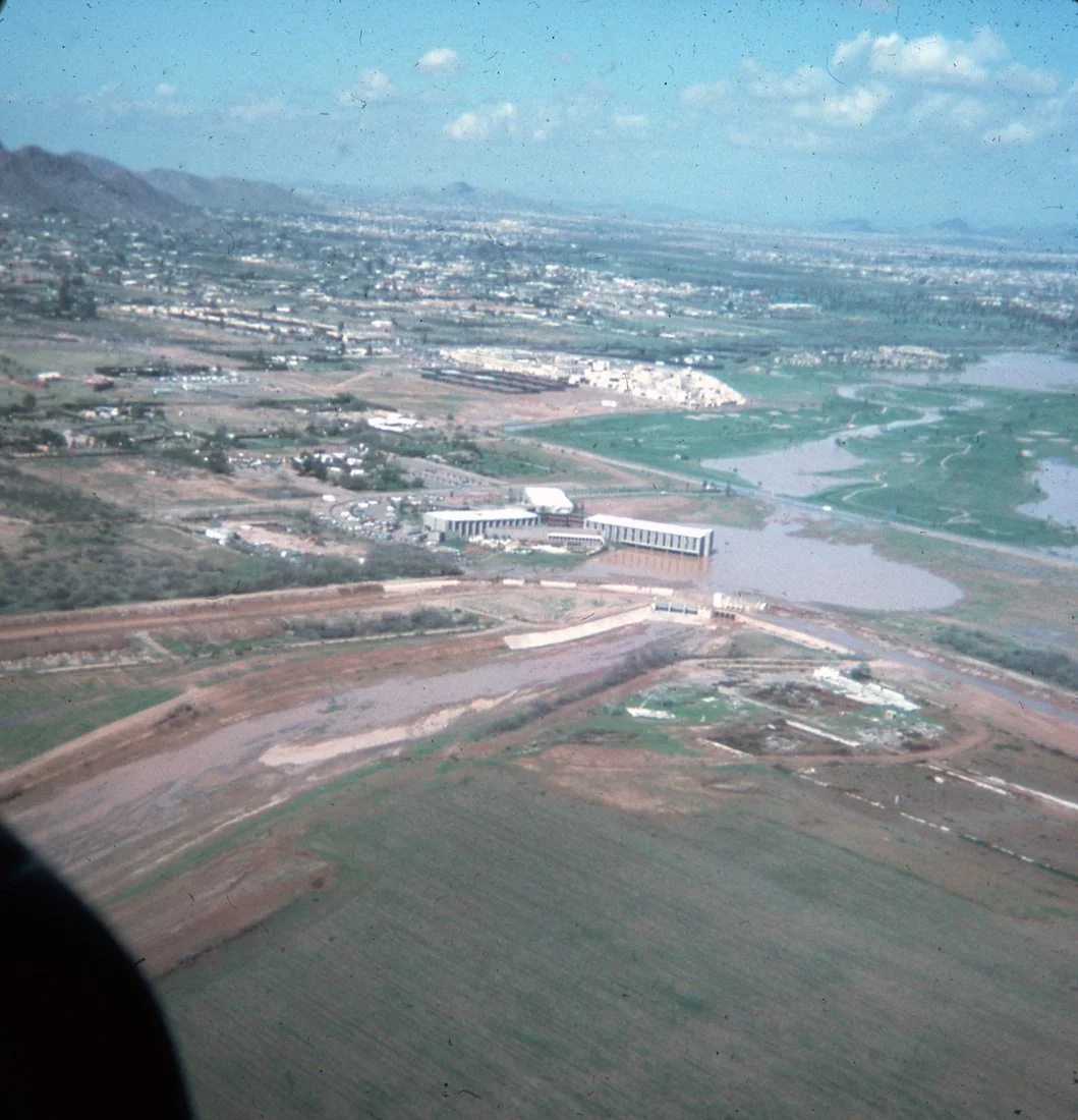 Aerial view of a landscape with mountains, rivers, and fields, showing a city or town in the distance.