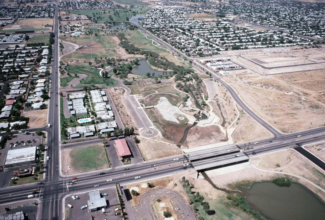 Aerial view of a city with a park, residential and commercial buildings, and highways crossing through the area.
