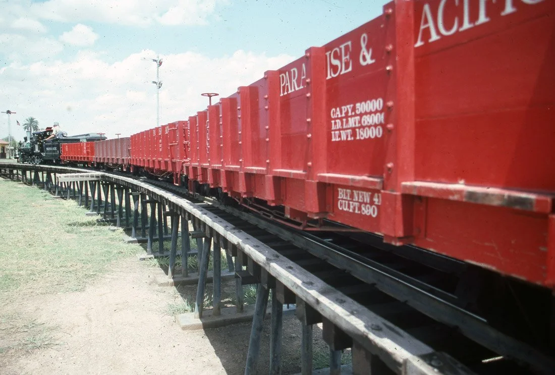 A vintage train with red freight cars on a curved track outdoors on a sunny day.