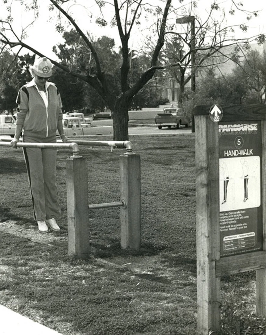 A woman on a treadmill at a park, with parked cars and trees in the background.