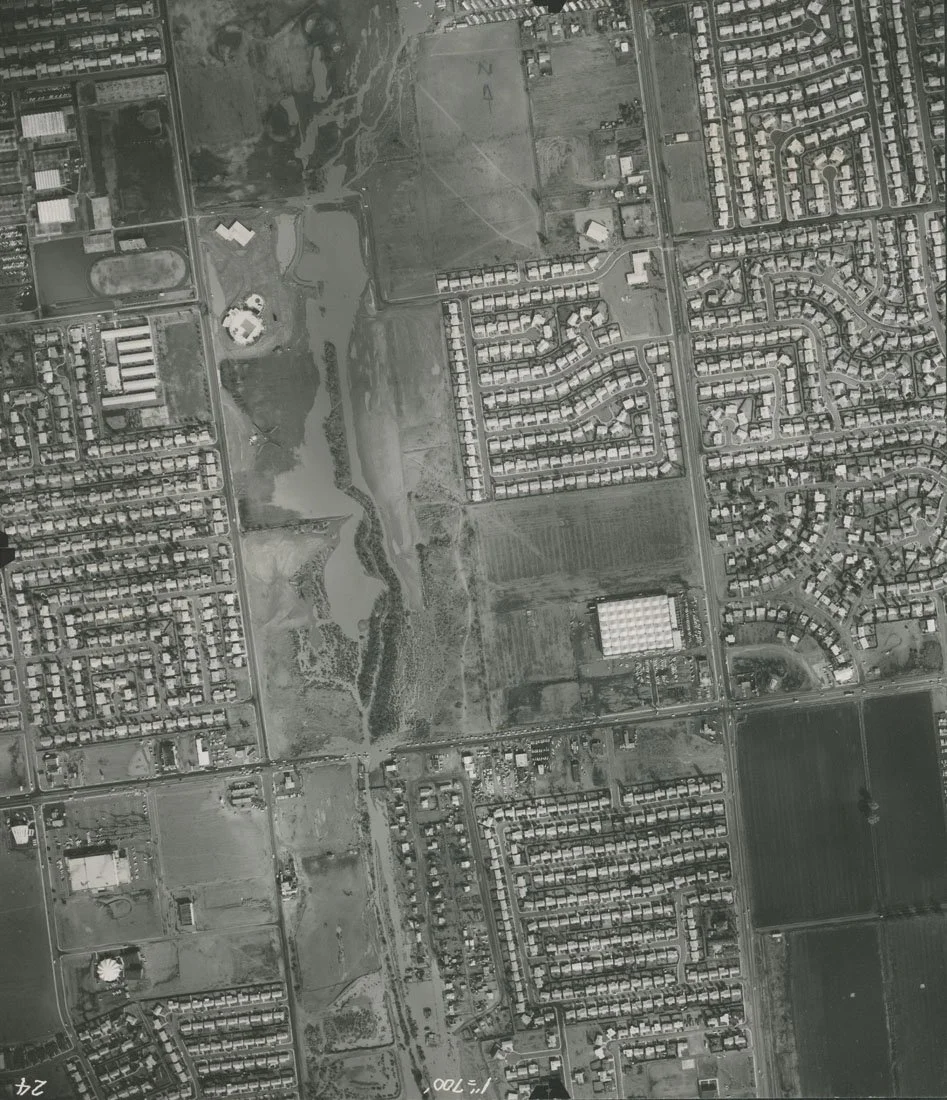 Aerial view of a suburban area with residential neighborhoods, a golf course, a body of water, and several large buildings on a grayscale image.