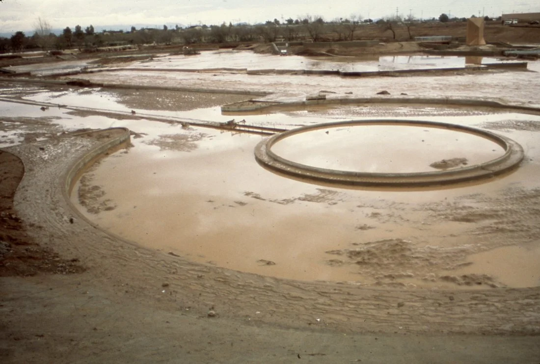 Dried salt flats with circular salt ponds and dirt roads, under a cloudy sky.