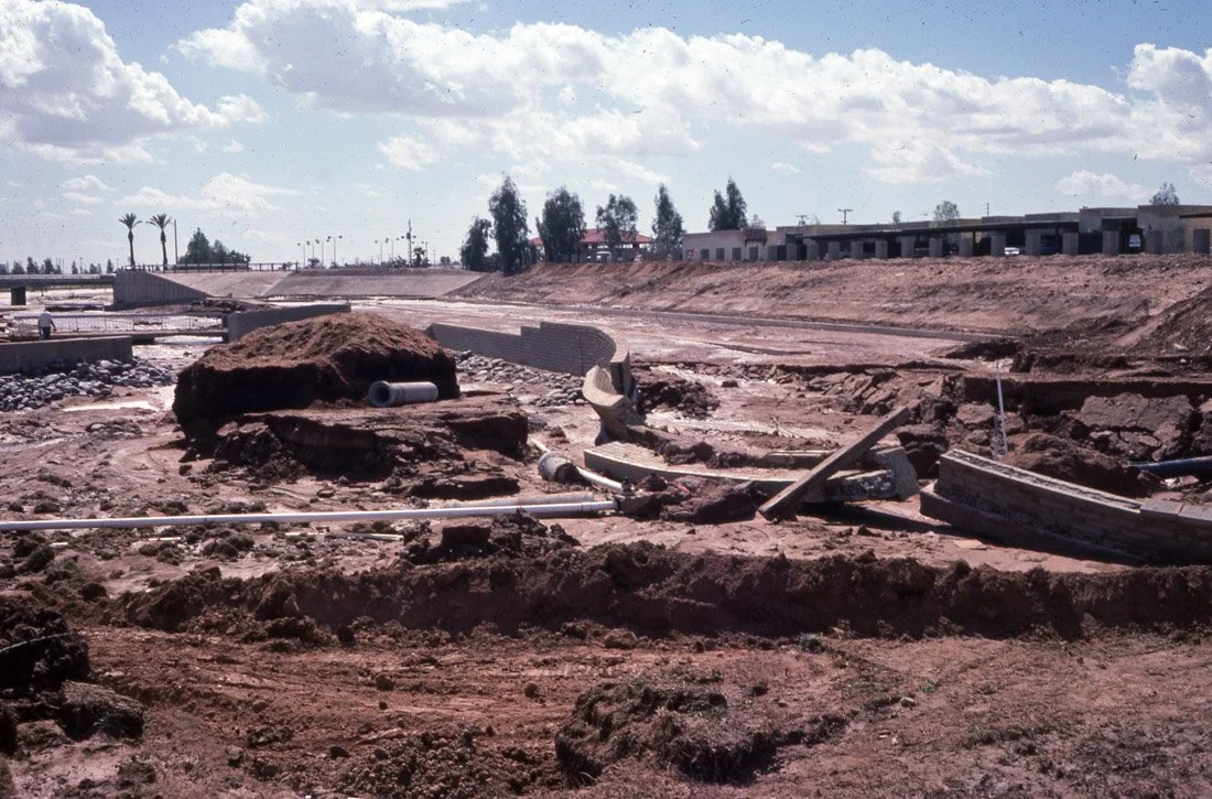 Construction site with dirt, pipes, and debris under a partly cloudy sky.