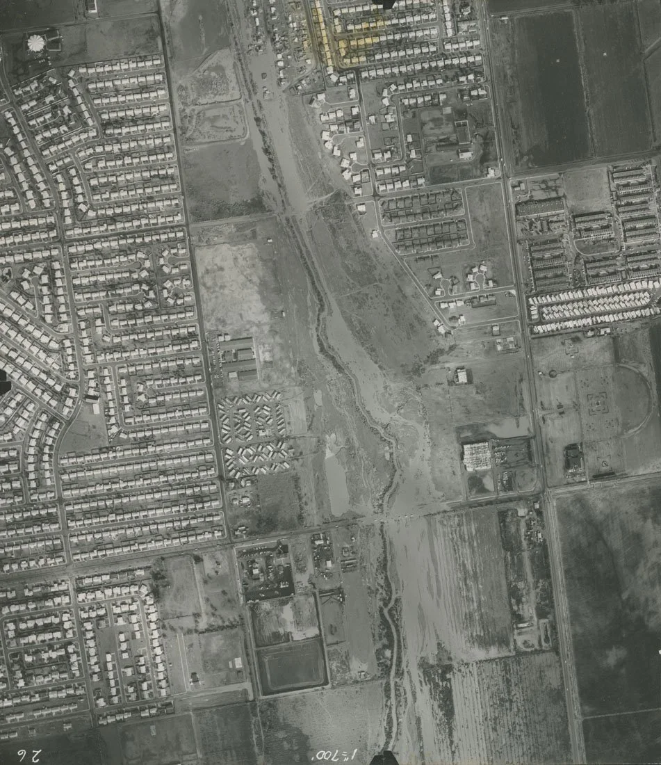 Aerial view of a suburban area with residential neighborhoods, open fields, and a waterway running through the center.