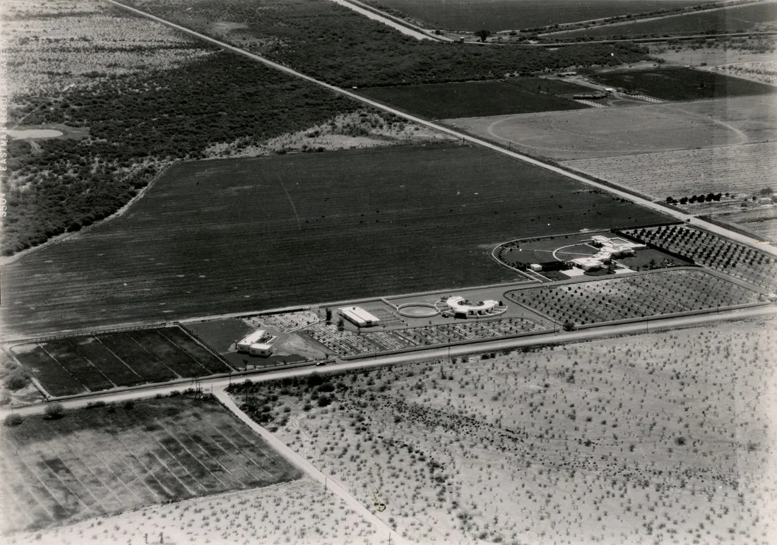 Aerial view of large agricultural fields with some buildings and structures, showing an expansive rural landscape.