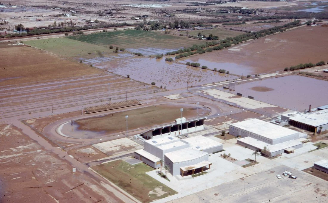 Flooded school campus with water covering fields and walkways, surrounding agricultural land and farmland.