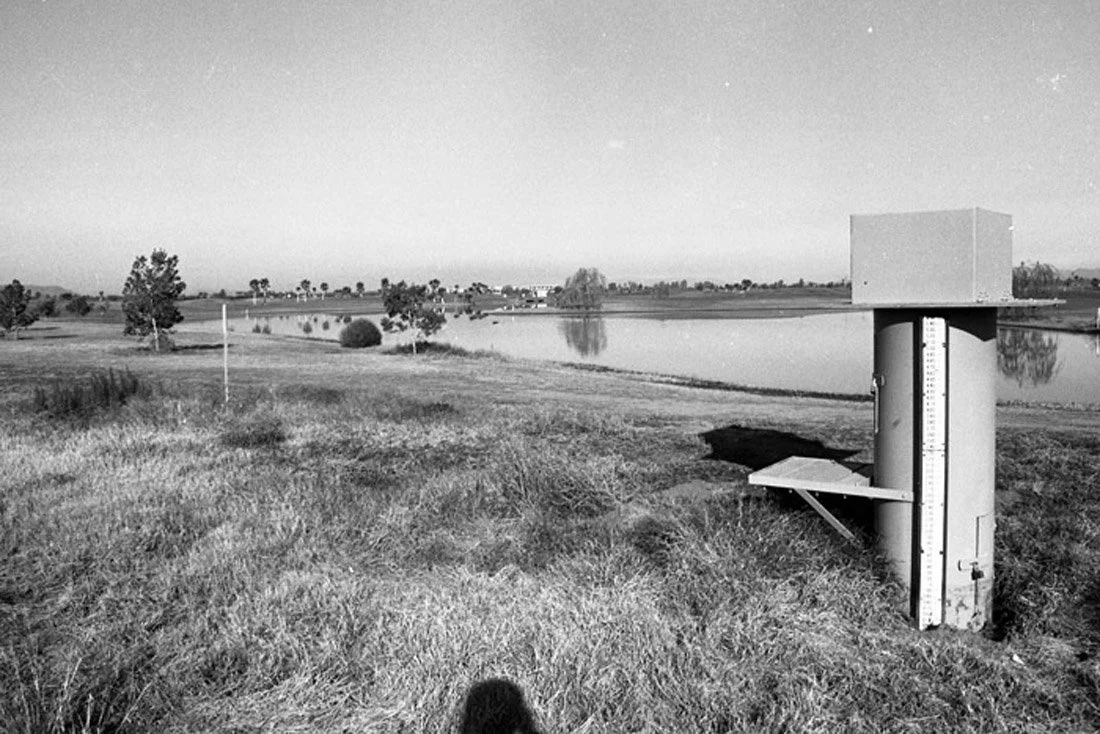 A golf course near a body of water with a weather station in the foreground.