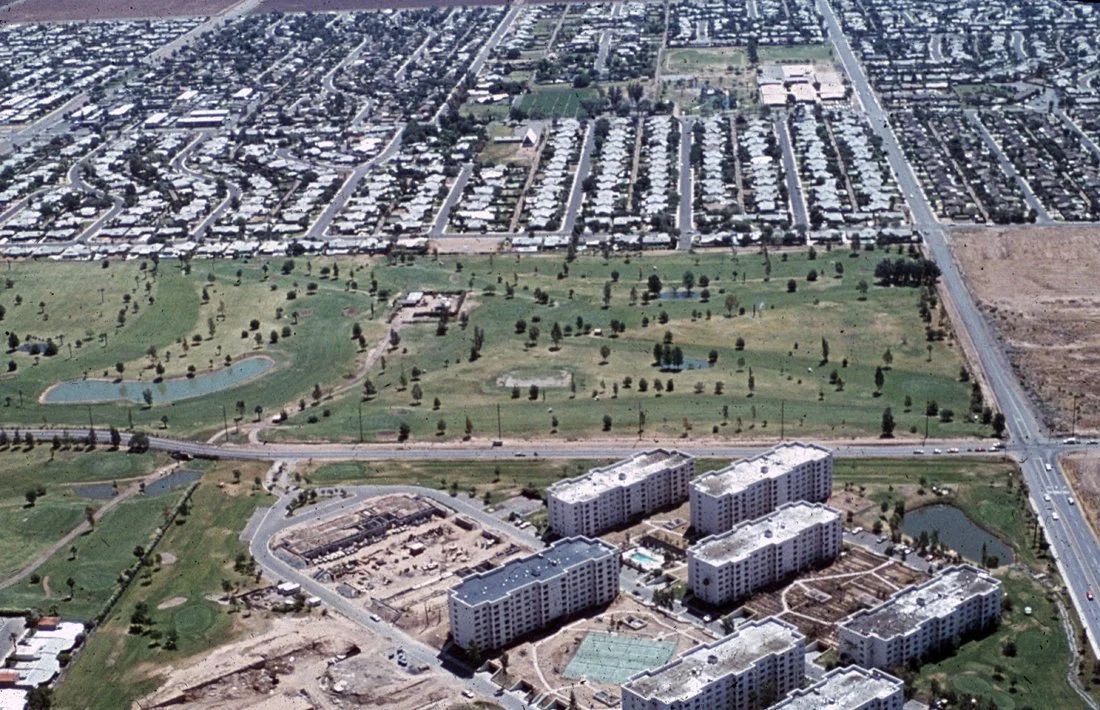 Aerial view of a suburban area with residential buildings, a park with ponds, and surrounding streets.