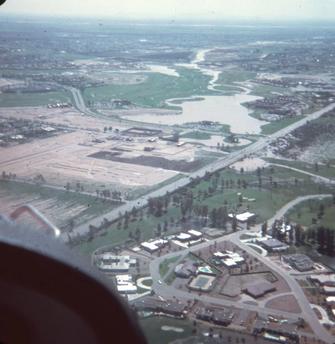 Aerial view of a landscape including a large lake, roads, residential and commercial buildings, and patches of green fields.