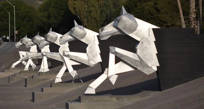 Large outdoor sculpture of stylized, geometric wolves sitting in a row on a slope.