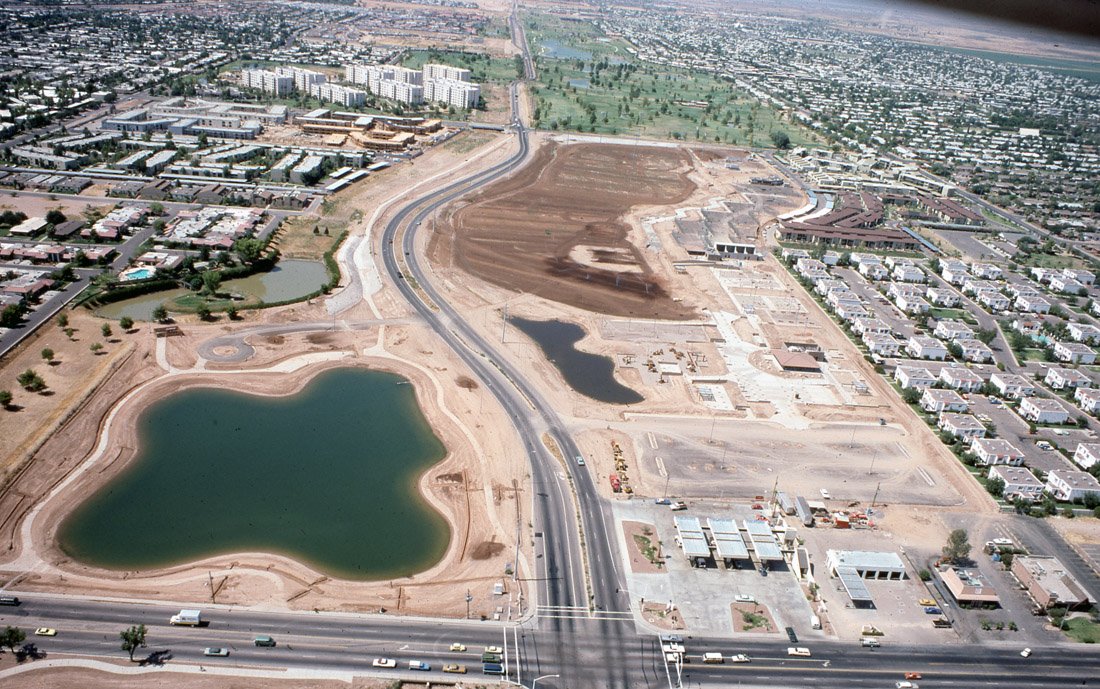 An aerial view of a developing urban area with construction sites, a lake, and residential neighborhoods.
