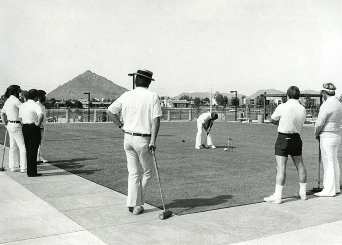 Group of people playing bocce ball outdoors with mountains in the background.