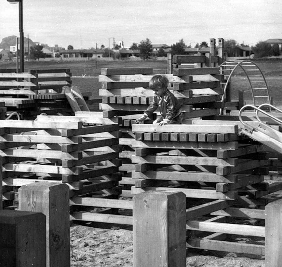 A young child playing on a large pile of wooden planks at a playground.