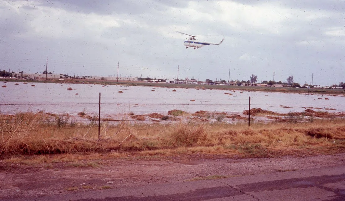 An airplane flying above a body of water with an overcast sky in the background.