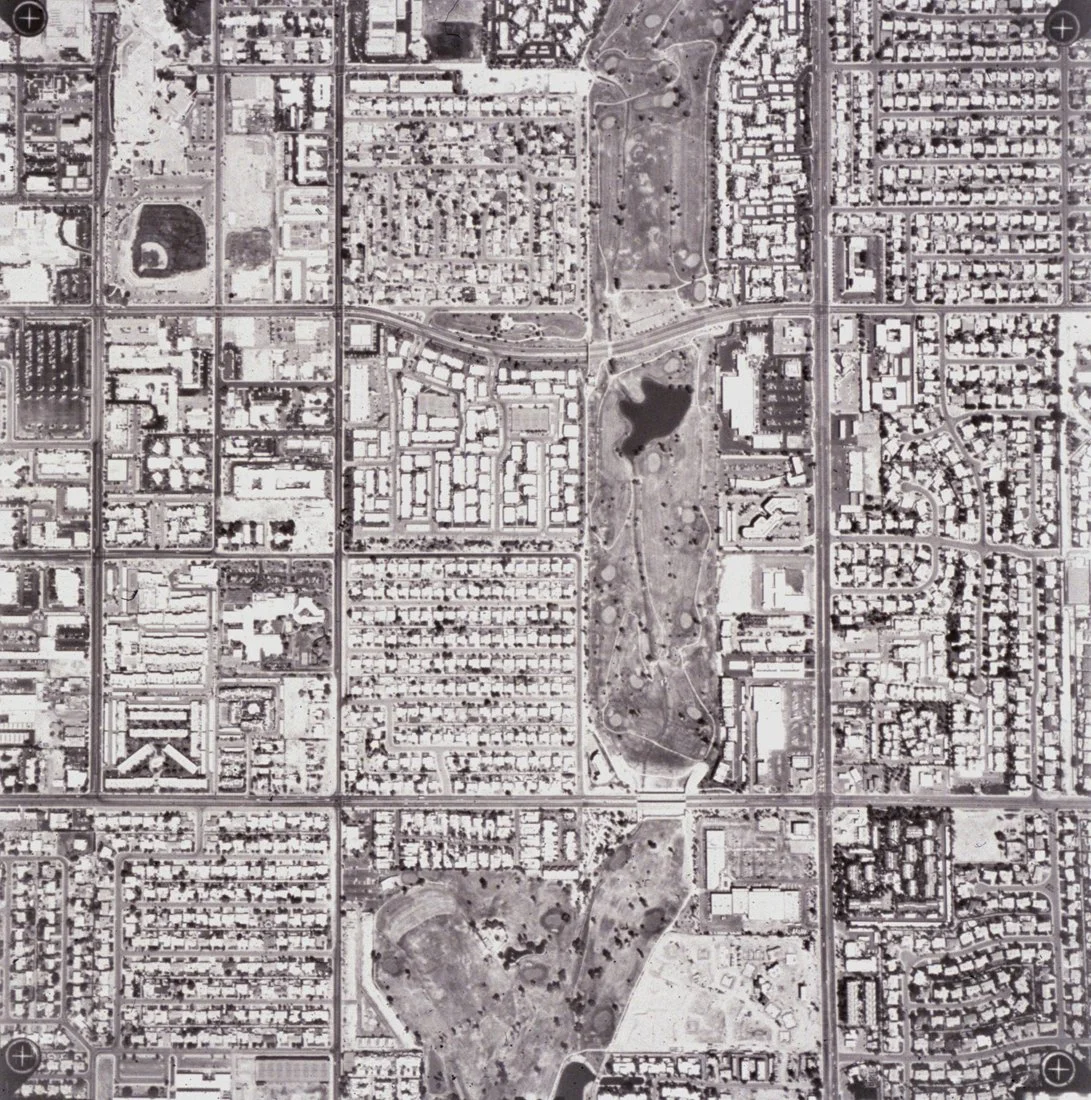 Aerial view of an urban park with walking paths, lakes, and surrounding residential neighborhoods in a city.