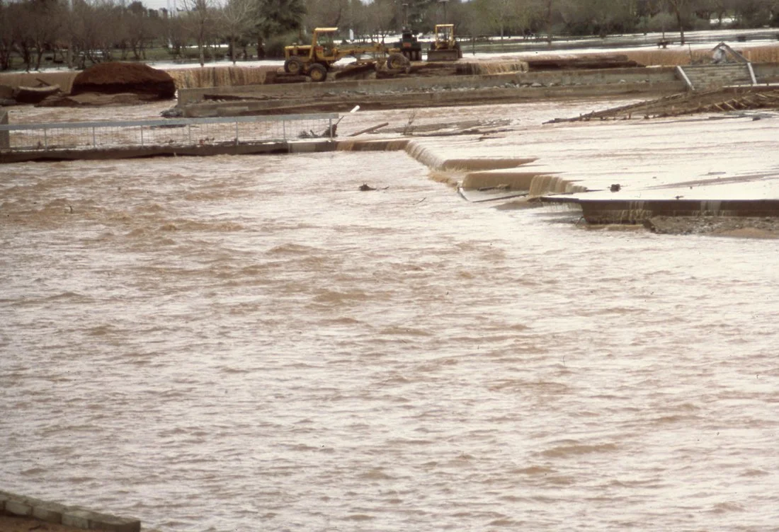 Flooded construction site with muddy water, construction equipment, and partially submerged structures.