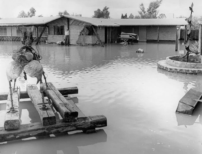 Flooded backyard with submerged deck, inflatables, and a house with a garage door open, set in a suburban area during daytime.