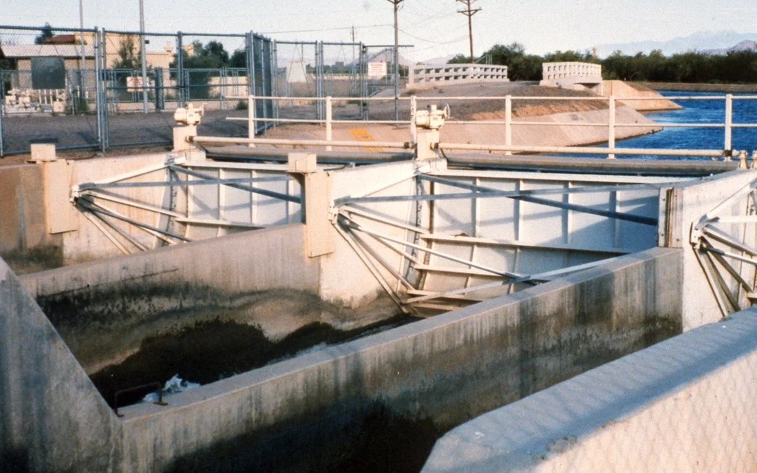 A water treatment plant with concrete basins, metal railings, and machinery for water processing.