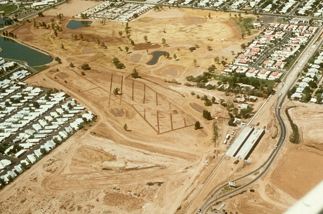 Aerial view of a large construction site with progress for a new stadium or arena, surrounded by residential neighborhoods, water bodies, and roads.