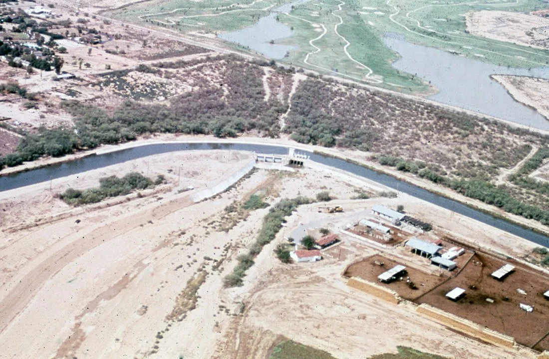 Aerial view of a dam and reservoir in a semi-arid area with some buildings and roads nearby.