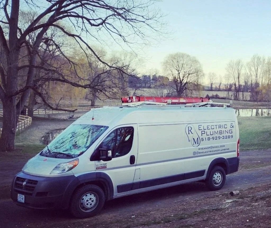 A white RM Electric & Plumbing service van equipped for electrical and plumbing repairs, parked in a rural Hudson Valley landscape.