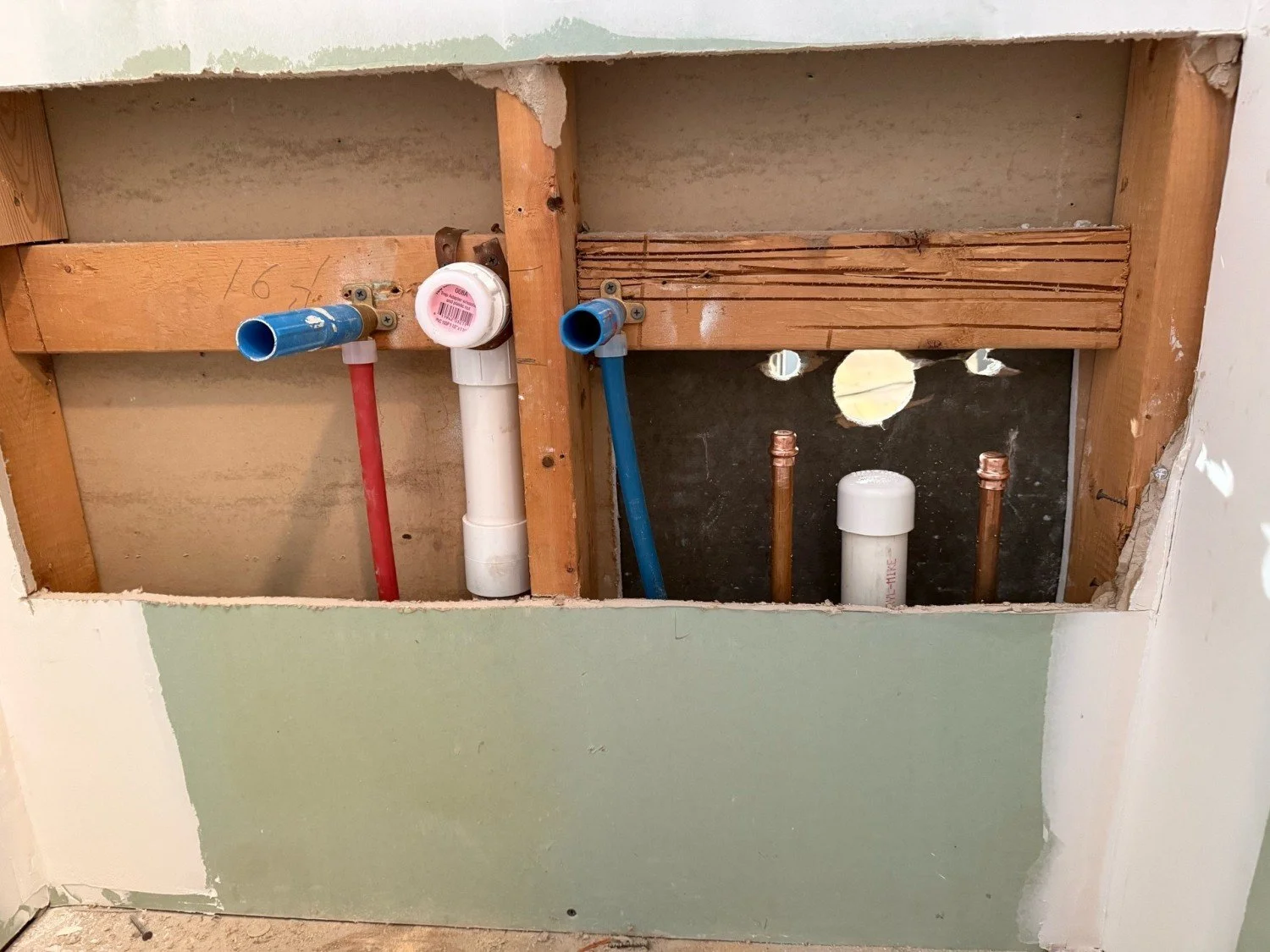 Professional plumbing rough-in by RM Electric & Plumbing, featuring color-coded PEX supply lines and a new PVC waste-and-vent stack for a home renovation.
