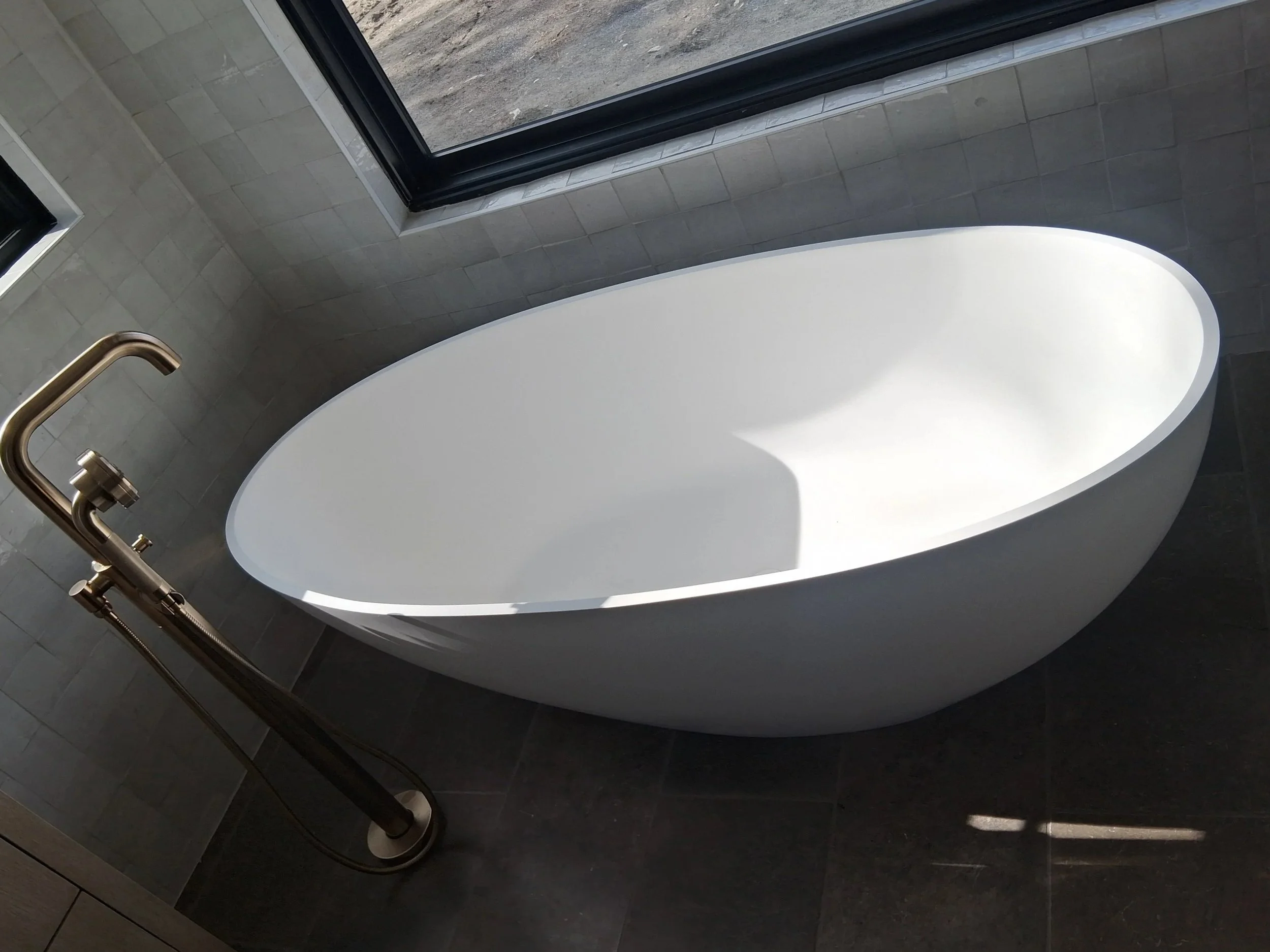 A modern freestanding soaking tub with a brushed gold floor-mounted faucet, installed by RM Electric & Plumbing as part of a high-end bathroom remodel.