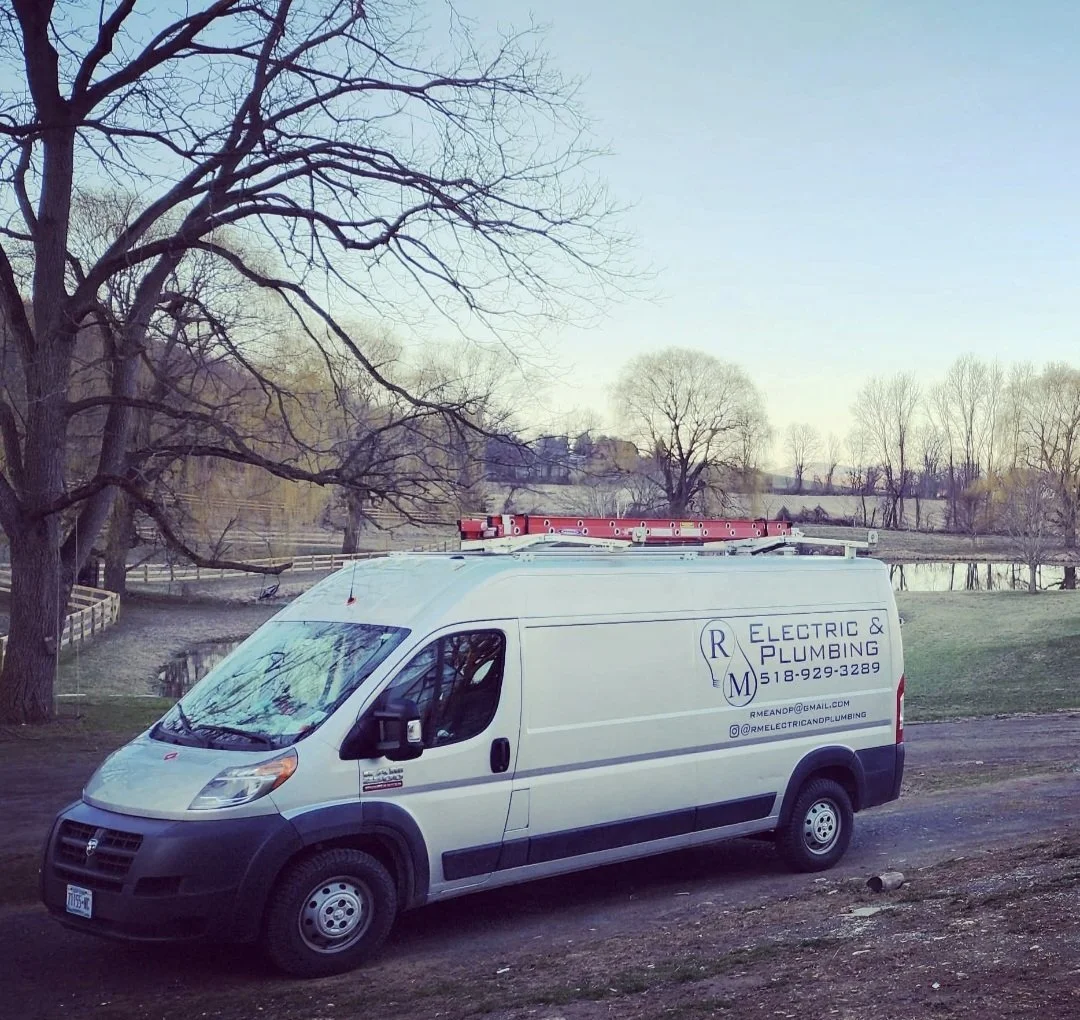 A white RM Electric & Plumbing service van equipped for electrical and plumbing repairs, parked in a rural Hudson Valley landscape.
